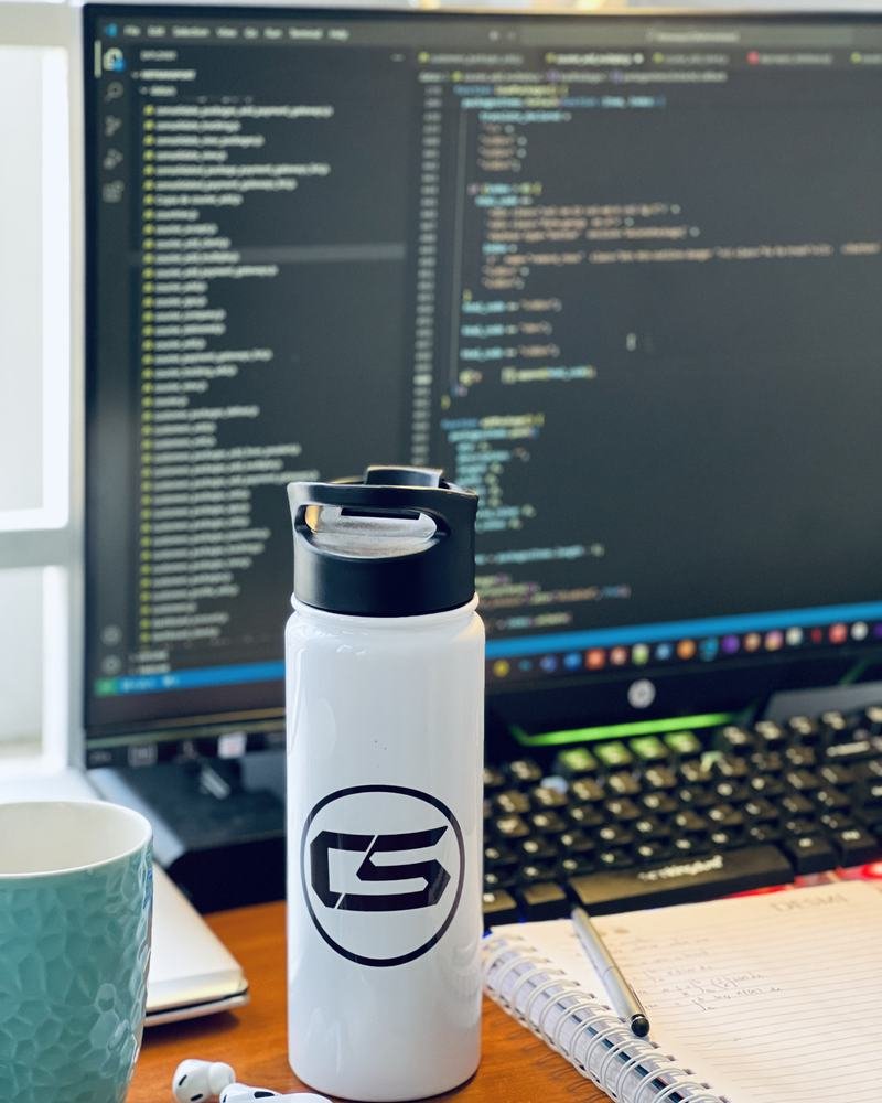 A developer's desk with code on screen and a CS water bottle