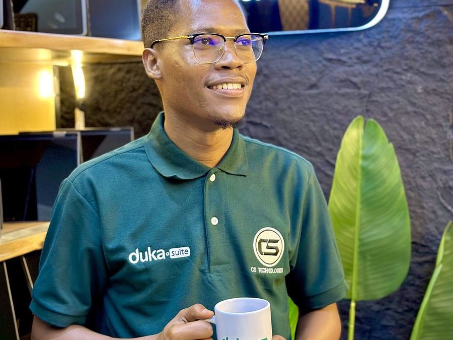 A smiling team member in a DukaSuite shirt holding a DukaSuite mug in the shop