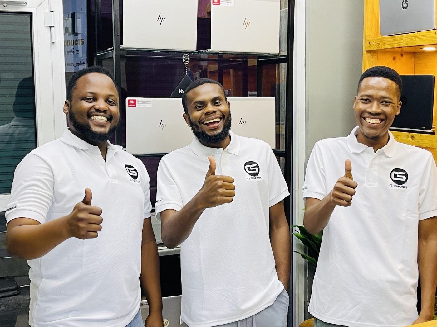 The CS Computers team in white shirts giving a thumbs up in the shop: the marketing manager, shop manager Thomas and a technician
